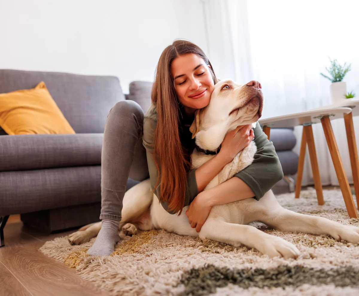 A woman embracing her dog on the living-room floor