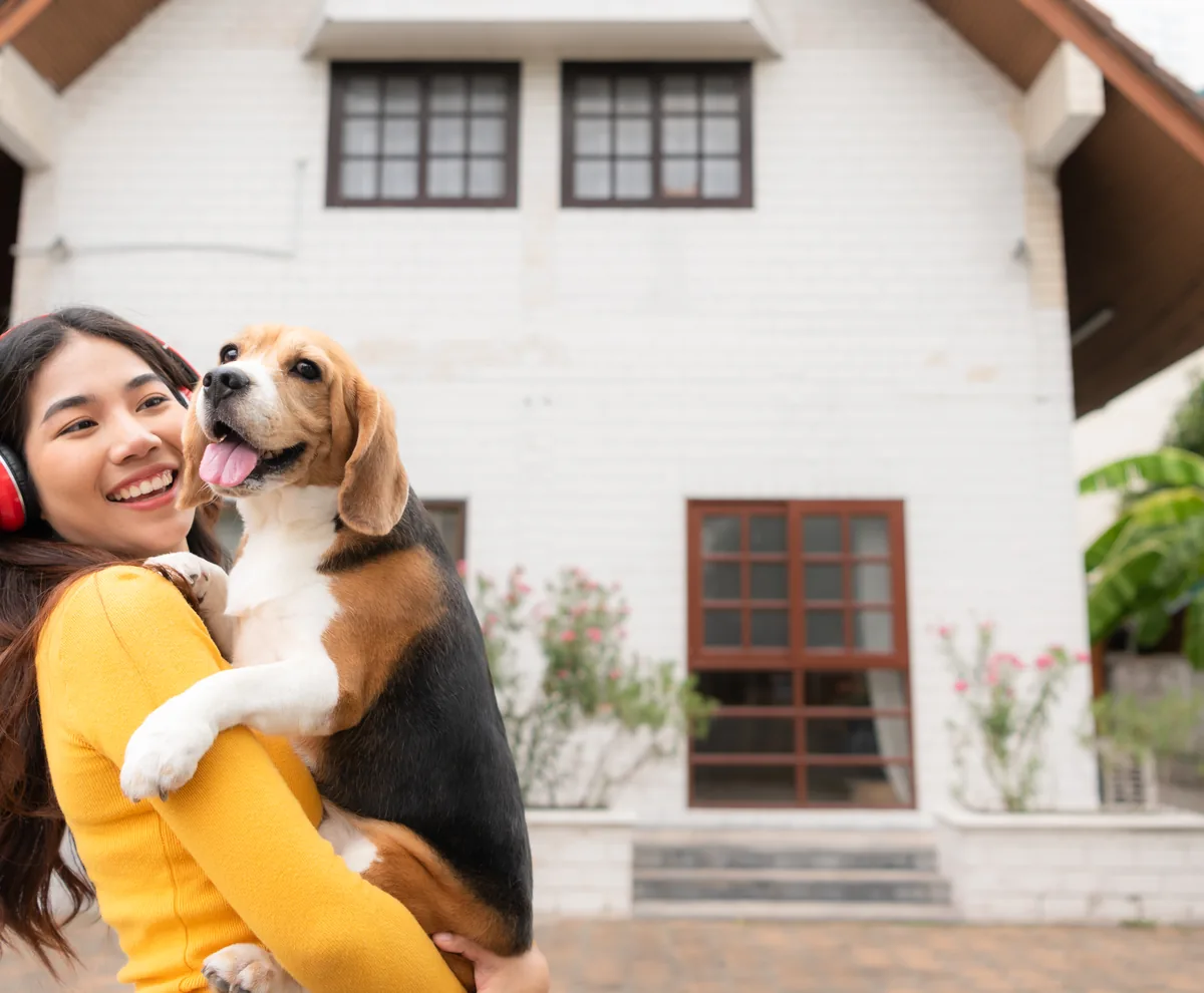 A woman cuddling her dog outside a suburban home
