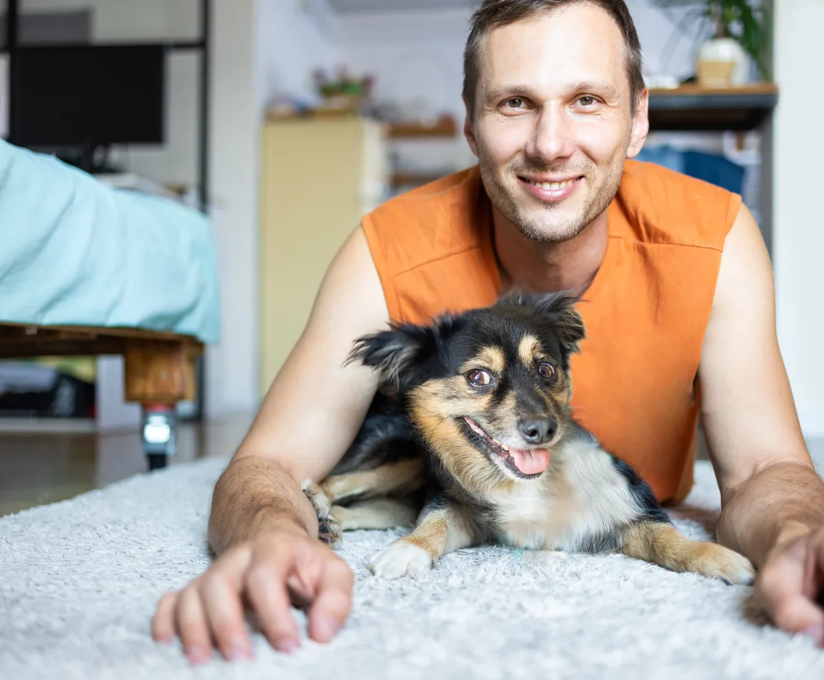 A man lying on a rug with his dog at home