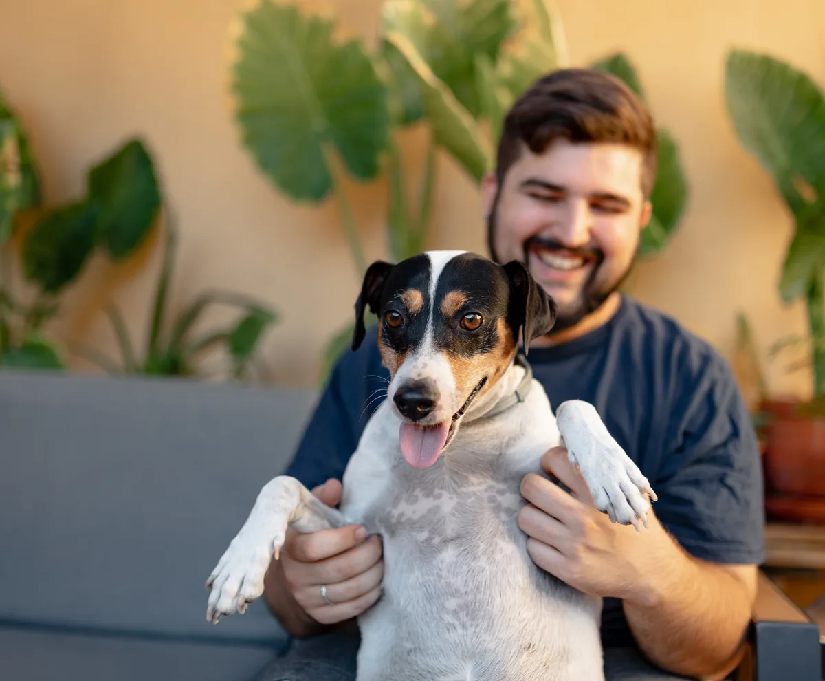 A man smiling as he holds his dog at home